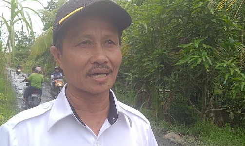 Kepala Desa Sepinggan Dahlan berlatar kondisi jalan yang rusak. 